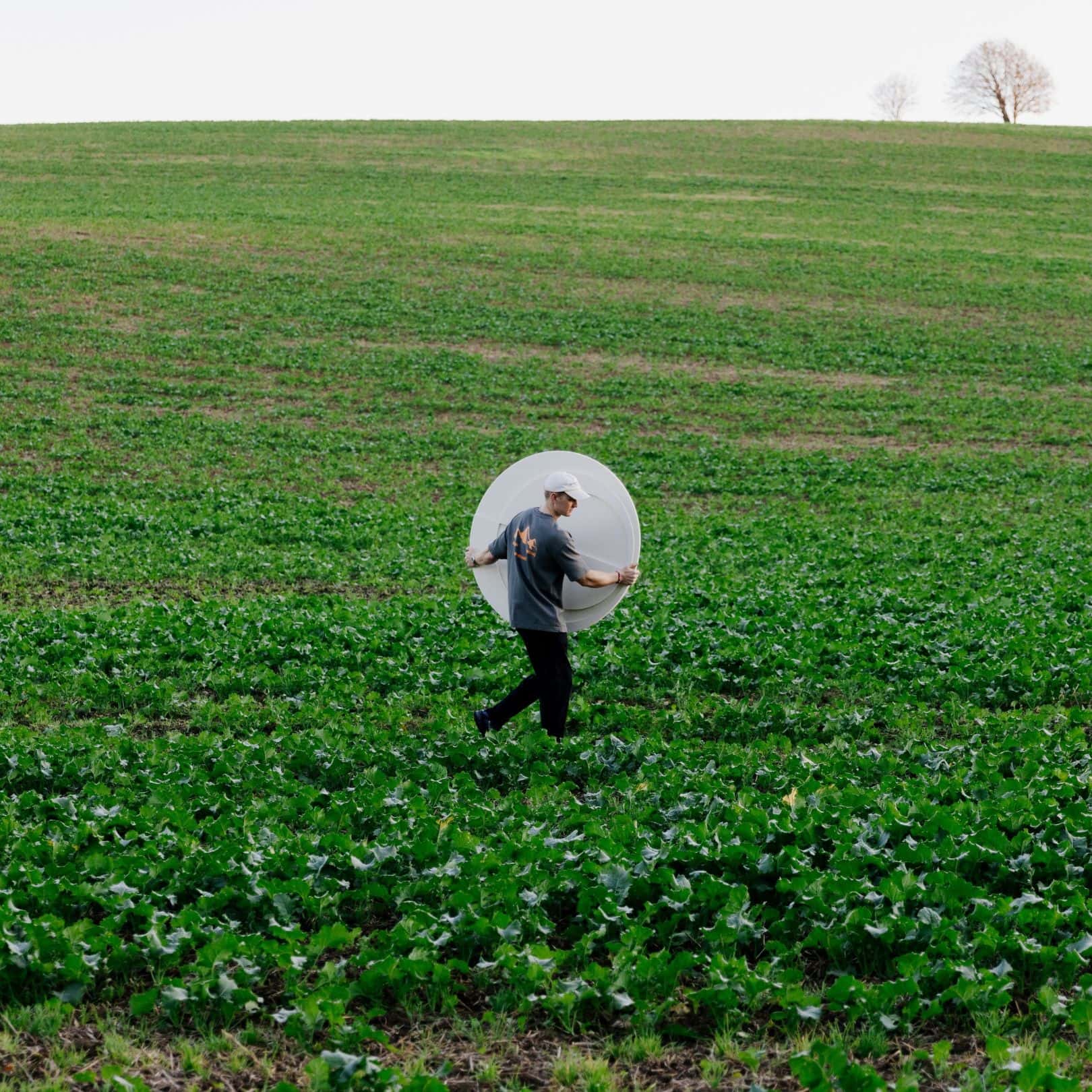 Man carrying Arturel acoustic artwork in an open field, blending art with nature in a green landscape setting.