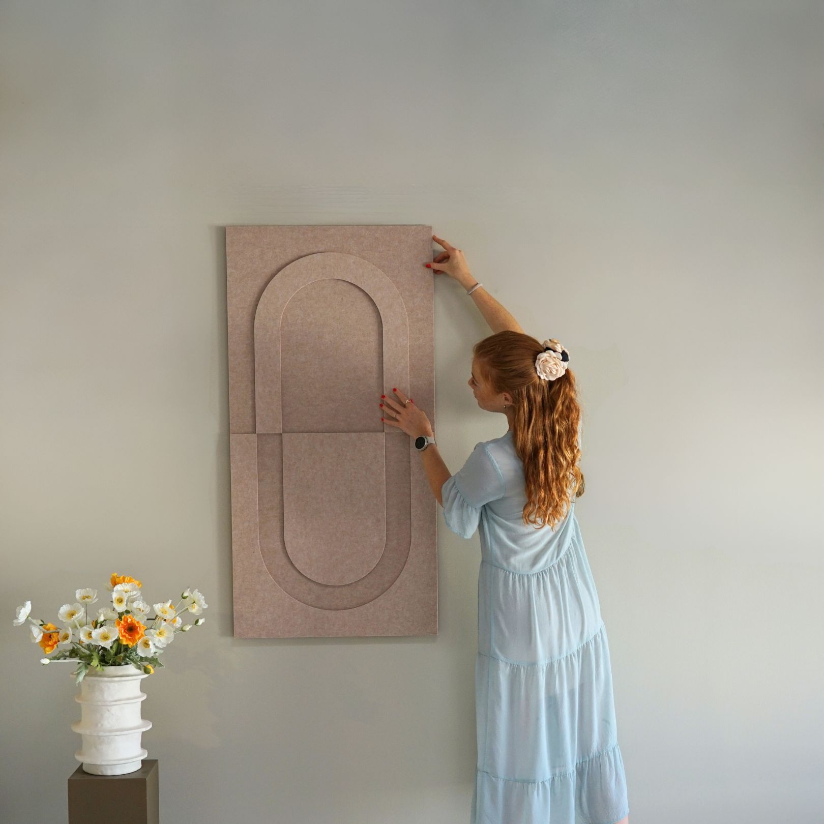 Woman installing beige geometric wall panel from Arturel, combining minimalist design with acoustic performance